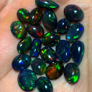 May include: A collection of black opal gemstones in various shades of green, blue, and red. The opals are pear-shaped and have a smooth, polished finish.