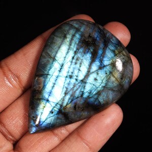 May include: A teardrop-shaped, polished labradorite gemstone with iridescent blue, green, and gold hues. The stone has a smooth, polished surface and a natural, irregular shape.