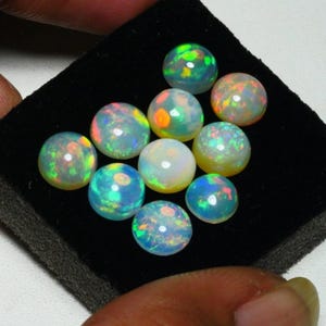May include: A collection of 10 round opal cabochons in various shades of green, blue, and white. The opals are displayed on a black velvet background.