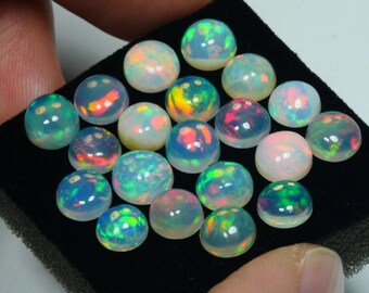 May include: A collection of 18 round, iridescent opal cabochons in various shades of white, blue, green, and red. The cabochons are displayed on a black velvet surface.