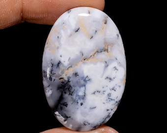 May include: Oval shaped cabochon of dendritic agate with a white, grey, and black pattern. The stone has a smooth, polished surface.