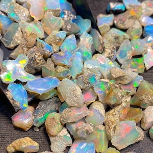 Puede incluir: Un montón de piedras preciosas de ópalo en bruto de varios tamaños y formas. Los ópalos son una mezcla de blanco, azul, verde y amarillo.