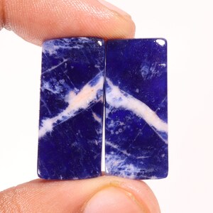 Puede incluir: Dos piezas rectangulares de sodalita azul con vetas blancas. Las piedras son lisas y pulidas.