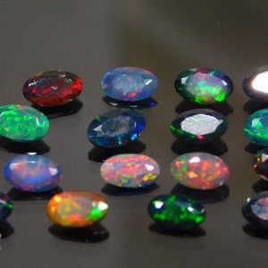 Könnte beinhalten: Eine Sammlung oval geschliffener Opale in verschiedenen Farben, darunter Rot, Blau, Grün und Schwarz. Die Opale werden auf einer reflektierenden schwarzen Oberfläche präsentiert, die ihr lebendiges Farbspiel zeigt. Jeder Stein ist einzigartig mit inneren Mustern und Blitzen.