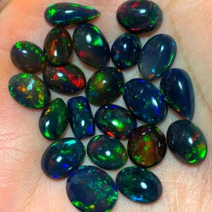 May include: A collection of black opal gemstones in various shapes and sizes. The opals have a dark base with flashes of green, blue, and red.