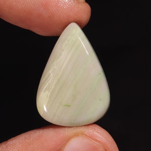 Pode incluir: Um cabochão de ágata verde e branca em forma de lágrima. A pedra é lisa e polida, com uma aparência translúcida.