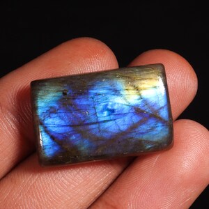 以下が含まれることがあります： 青、緑、金色の色合いの長方形の虹色のラブラドライトの宝石。石は磨かれており、滑らかな表面をしています。