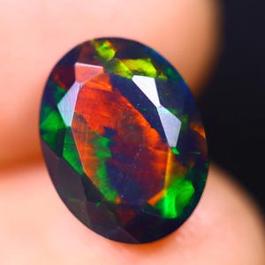 Puede incluir: Una piedra preciosa de ópalo ovalada facetada de color verde oscuro, rojo y negro.