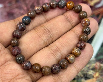 May include: A beaded bracelet featuring a variety of earth-toned gemstones. The bracelet's beads are primarily brown, with accents of red, orange, and blue. The round beads are strung together, creating a bracelet that is approximately 7 inches in circumference.