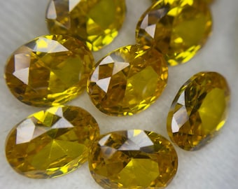 May include: A collection of faceted, oval-shaped yellow gemstones. The gems have a brilliant cut, reflecting light and creating a sparkling effect. The stones are a warm, golden yellow color, and are likely used for jewelry making or collecting.