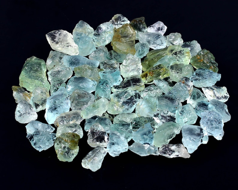 May include: A large pile of aquamarine gemstones, with a variety of shapes and sizes. The stones are a light blue-green color and have a translucent appearance.
