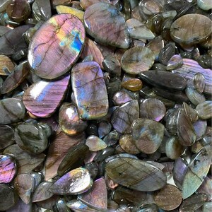 May include: A collection of polished labradorite gemstones in various shapes and sizes. The stones display a range of colors, including purple, blue, and green, with iridescent flashes. The gemstones are oval, teardrop, and irregular shapes.