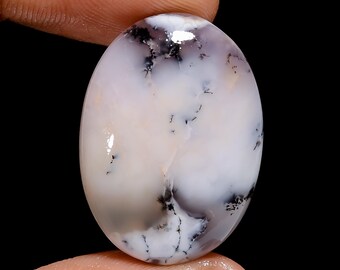 May include: A white oval cabochon with black dendritic inclusions. The stone has a smooth, polished surface and is translucent.