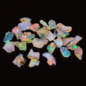 Könnte beinhalten: Eine Sammlung von rohen, natürlichen Opal-Edelsteinen. Die Opale sind in verschiedenen Weißtönen gehalten und zeigen schimmernde Farbschattierungen, darunter Grün, Blau und Rot.