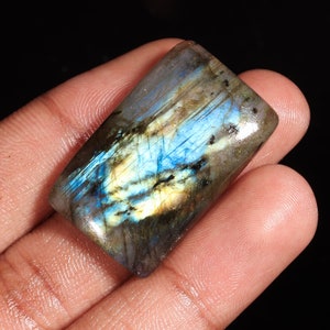 May include: A rectangular, iridescent labradorite gemstone with blue, green, and gold hues. The stone is polished and has a smooth surface.