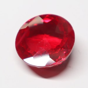 May include: A bright red, round, faceted gemstone with a high polish.
