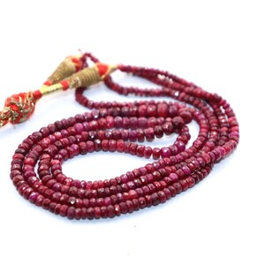 May include: A strand of red ruby beads with a gold tassel. The beads are faceted and have a slightly irregular shape.