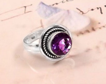 May include: A silver ring with a purple amethyst gemstone set in a decorative bezel. The ring is marked "925" on the inside band.