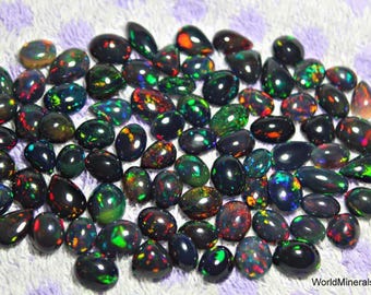 May include: A collection of black opal gemstones in a teardrop shape. The opals have a variety of iridescent colors, including green, red, and blue.