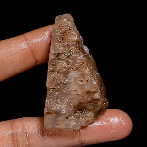 May include: A rough, translucent, brown and white crystal with a pointed top. The crystal has a layered, striated appearance.