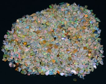 May include: A large pile of small, iridescent opal chips in various shades of white, green, and yellow. The chips are scattered on a black surface.