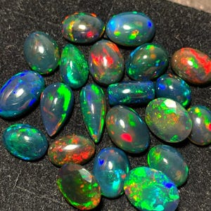 May include: A collection of 18 black opal gemstones in various shapes and sizes. The opals have a dark base with flashes of green, blue, red, and yellow.