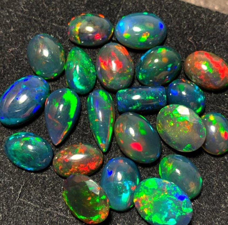 May include: A collection of 18 black opal gemstones in various shapes and sizes. The opals have a dark base with flashes of green, blue, red, and yellow.