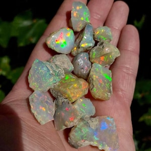 May include: A collection of rough opal stones in various shades of green, blue, and red. The stones are iridescent and have a natural, unpolished finish.