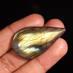 May include: A teardrop-shaped labradorite gemstone cabochon with a golden sheen and iridescent blue and green flashes.