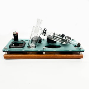 May include: A glass water pipe with a glass bowl and a wooden base. The pipe is sitting on a glass tray with a lighter and a small ashtray.