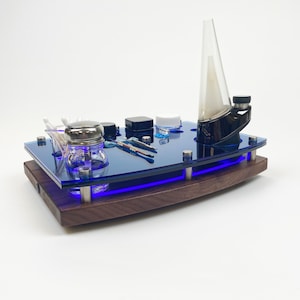 May include: A rectangular wooden base supports a blue acrylic platform illuminated by blue LED lights. The platform holds a glass cone-shaped device, a small glass jar with a metal lid, cotton swabs, and various small tools in designated cutouts.