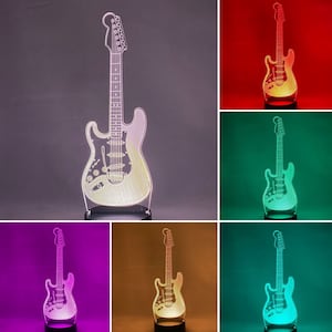 May include: A 3D printed acrylic guitar lamp with a clear body and a black base. The lamp is shown lit up in different colors, including red, green, blue, purple, orange, and white.