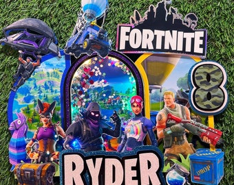 May include: A Fortnite themed birthday cake topper with a blue and white hot air balloon, a green camouflage number 8, a blue and white character with a pink and white outfit, a black character with a purple outfit, a brown character with a blue and white shirt, a purple and black glider, a blue and white truck, a blue and white chest, a blue box with the word "DROP" on it, and a blue and white name banner that says "RYDER".