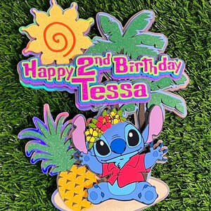 May include: A blue Stitch character from the Disney movie Lilo & Stitch wearing a red shirt and a flower crown. Stitch is sitting on a beach with a pineapple and a palm tree behind him. The text "Happy 2nd Birthday Tessa" is in the background.