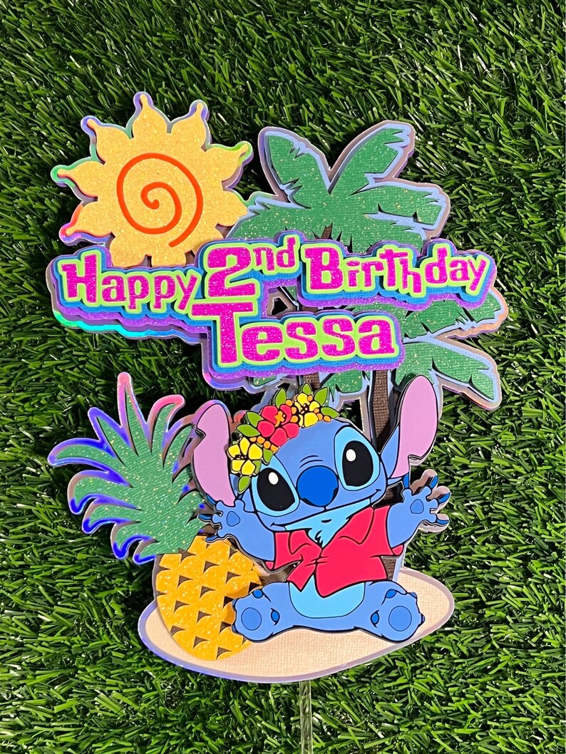 May include: A blue Stitch character from the Disney movie Lilo & Stitch wearing a red shirt and a flower crown. Stitch is sitting on a beach with a pineapple and a palm tree behind him. The text "Happy 2nd Birthday Tessa" is in the background.
