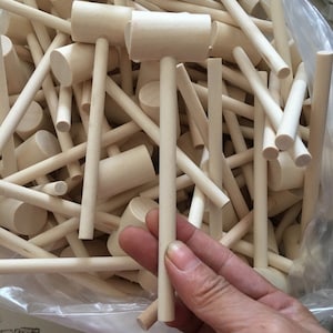 May include: A collection of small, unfinished wooden mallets. Each mallet has a cylindrical handle and a rectangular head. The mallets are made of light-colored wood and appear to be new. The image shows a close-up view of the mallets.