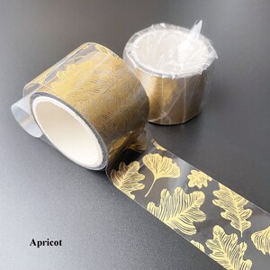 May include: Two rolls of gold leaf patterned washi tape. The tape is transparent with a black background and gold leaf pattern. The text "Apricot" is visible in the bottom left corner of the image.
