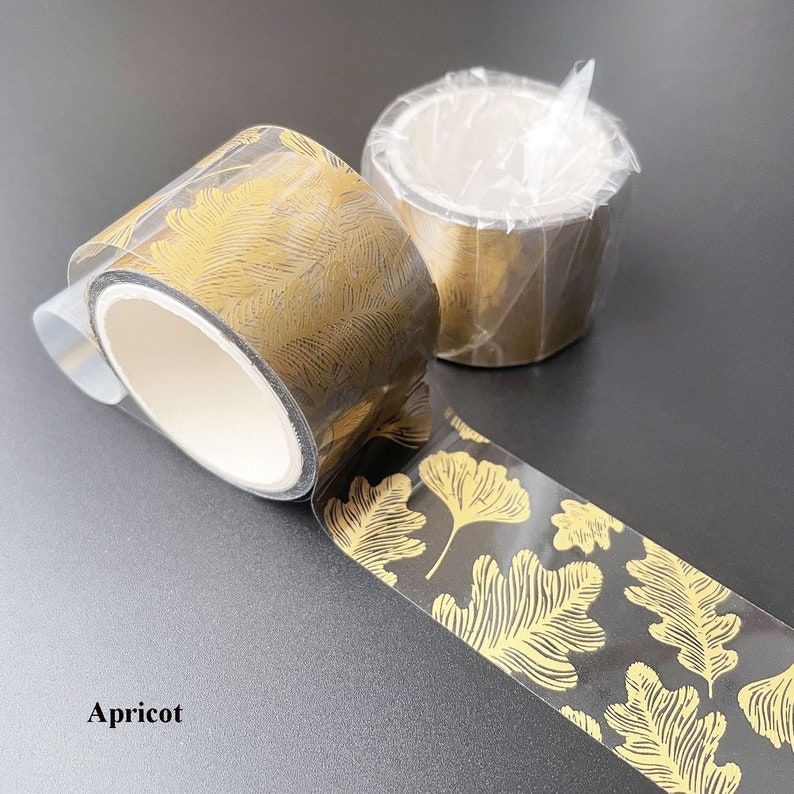 May include: Two rolls of gold leaf patterned washi tape. The tape is transparent with a black background and gold leaf pattern. The text "Apricot" is visible in the bottom left corner of the image.