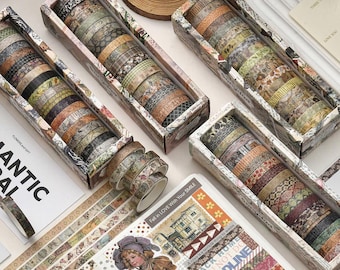 May include: A collection of decorative washi tape rolls in various patterns and colors, including floral, geometric, and vintage designs. The tape is arranged in rectangular boxes and displayed with decorative paper and stickers. The text "Fall in LOVE With Your SMILE" is visible.