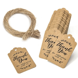 Può includere: Un insieme di etichette regalo in carta kraft con la scritta "Thank You" in corsivo nero, accompagnate da un rotolo di spago. I tag hanno un bordo smerlato decorativo e sono progettati per festeggiare con gli altri.