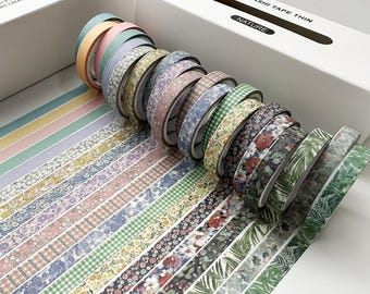 May include: A set of 18 washi tapes in a variety of floral and geometric patterns. The tapes are arranged in a fan shape and are labeled "Washi Tape Thin Nature".