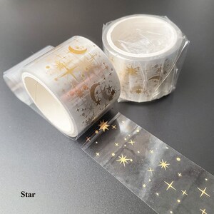 May include: Two rolls of clear washi tape with gold foil stars, moons, and dots. The tape is labeled "Star".
