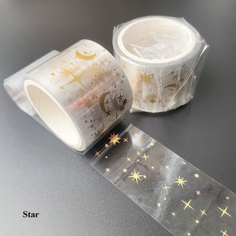 May include: Two rolls of clear washi tape with gold foil stars, moons, and dots. The tape is labeled "Star".