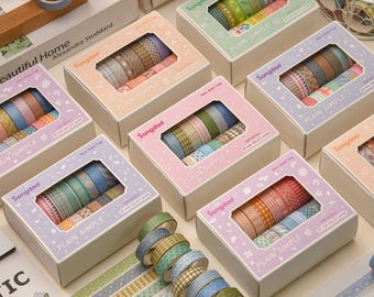 May include: Assortment of decorative washi tape rolls in various colors and patterns, displayed in boxes with the text "PLAIN SIMPLE" and "Songdad". Some rolls are stacked, showcasing the different designs. Ideal for crafts and stationery.