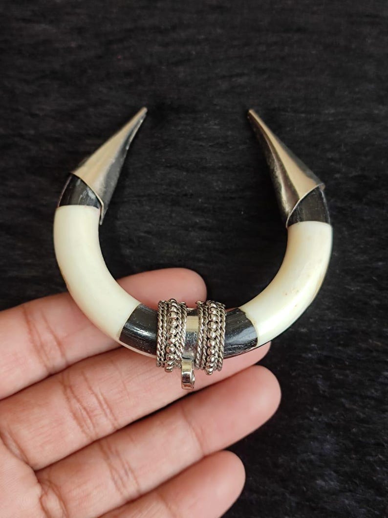 May include: A handcrafted, U-shaped pendant featuring a cream-colored, curved base with black accents. The ends are capped with silver-colored metal, and the center is adorned with silver-toned chain detailing and a small pendant.