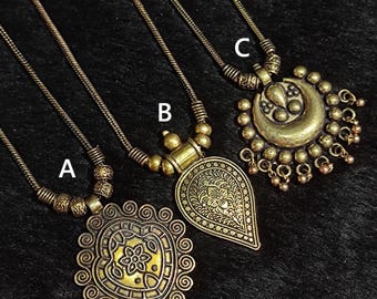 May include: Three antique gold-toned necklaces with intricate pendant designs. Necklace A features a heart-shaped pendant with a floral center. Necklace B has a teardrop-shaped pendant. Necklace C showcases a crescent moon pendant with dangling beads.