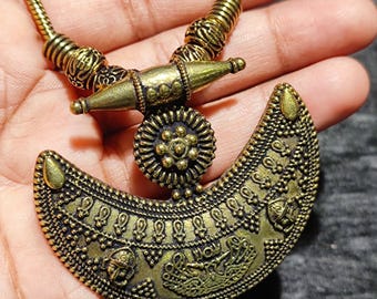 May include: Antique gold-colored necklace with a crescent-shaped pendant. The pendant features intricate embossed patterns and a central floral design. The necklace has a textured chain and a decorative clasp, showcasing an ethnic or bohemian style.