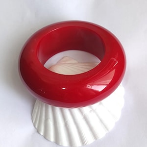 Op de afbeelding: Een dikke, glanzende, effen rode armband met een glad, afgerond oppervlak. De armband is cirkelvormig en heeft een hoogglanzende afwerking die het licht reflecteert op de levendige rode kleur, wat zorgt voor een opvallend accessoire.
