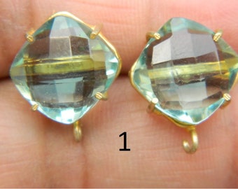 May include: A pair of gold-tone earrings with light blue faceted glass stones. The stones have a gold-tone band around the center. The earrings have a hook closure.