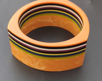 Peut inclure: Un bracelet-jonc à rayures multicolores avec une finition orange marbrée. Le bracelet est en plastique et a une forme géométrique.